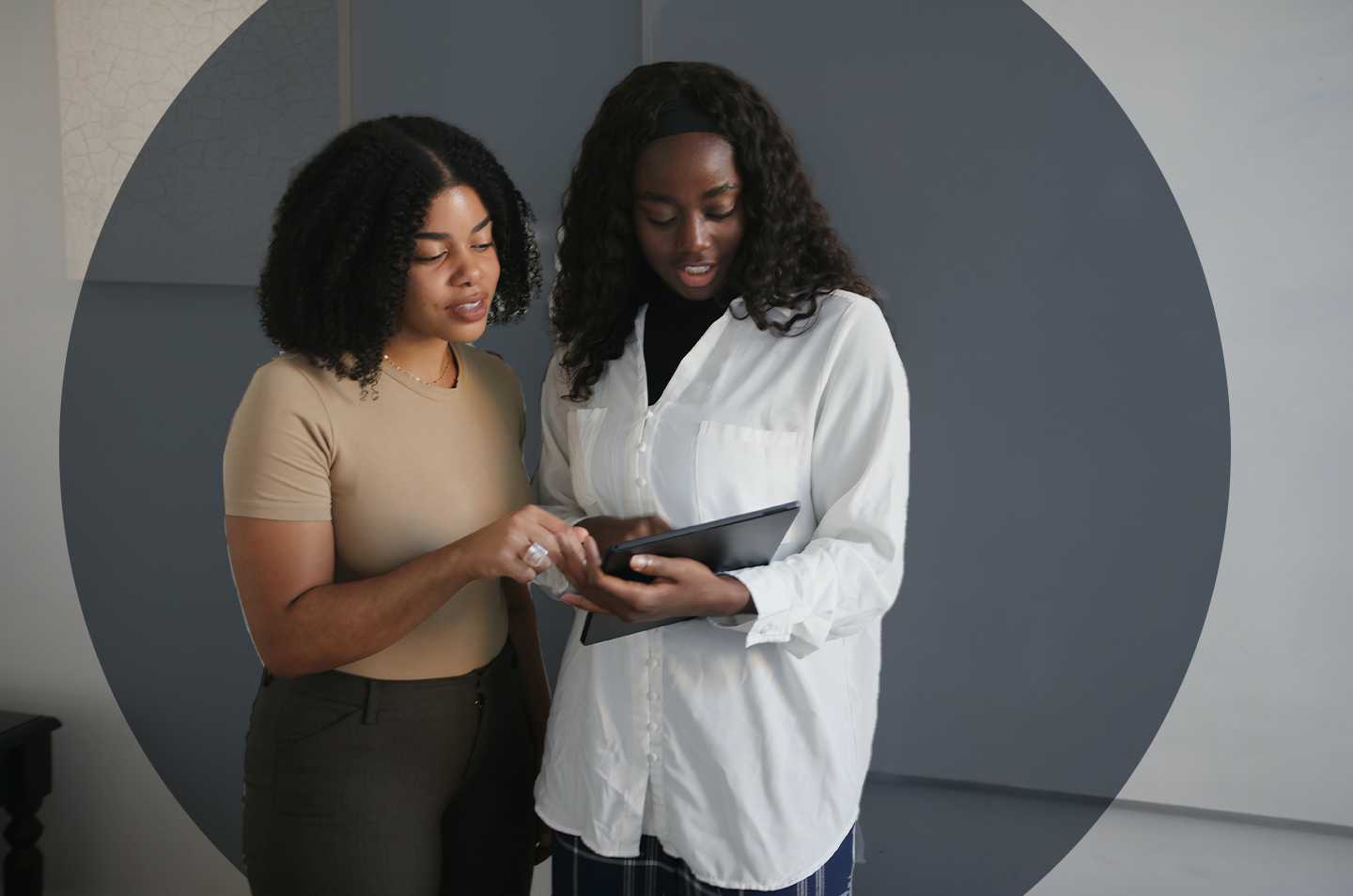 two women standing together looking at a tablet